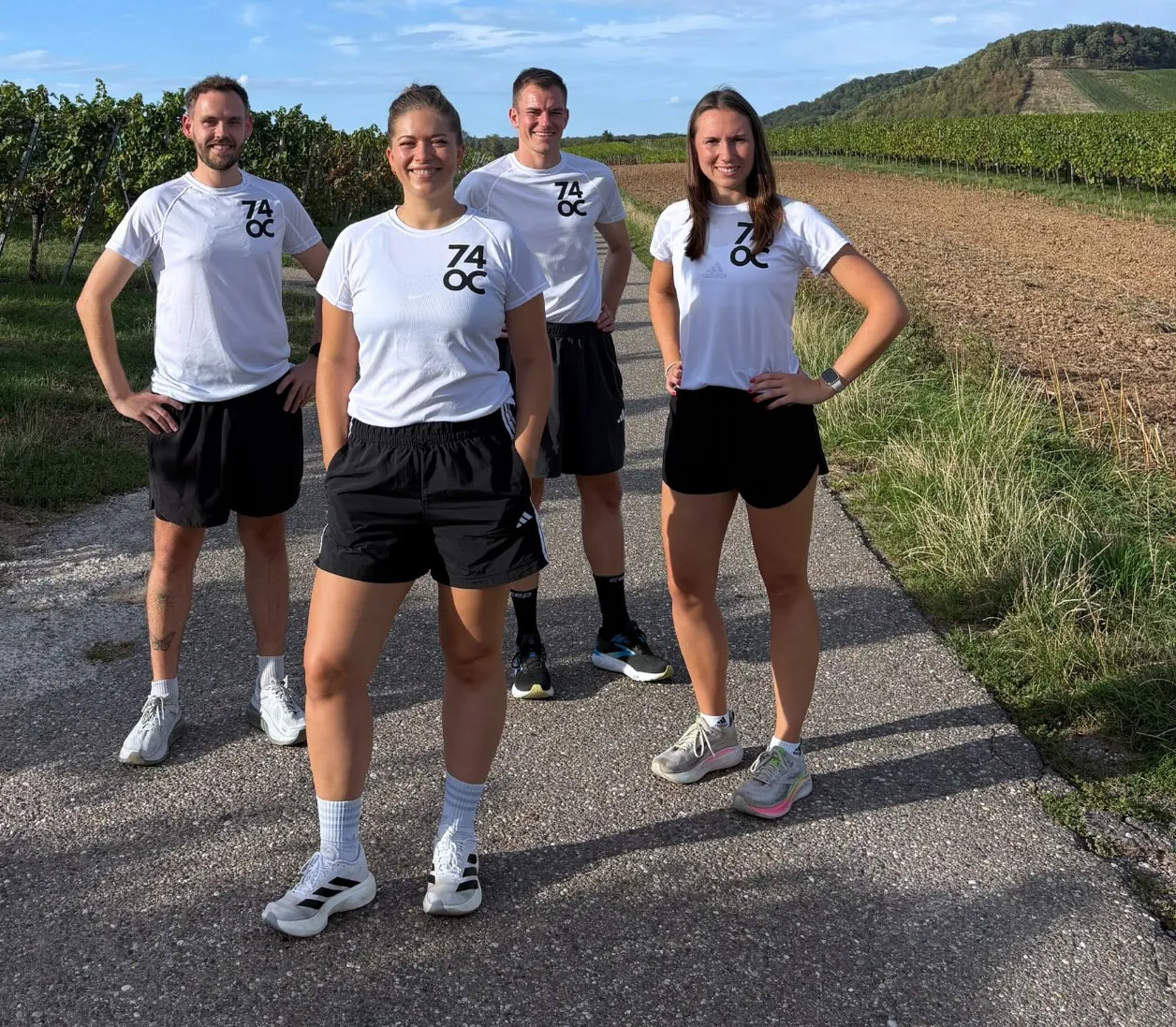 Die vier Coaches Simon, Jenny, Mari und Lisa im 74OC-Shirt auf einem Feldweg zwischen Weinbergen